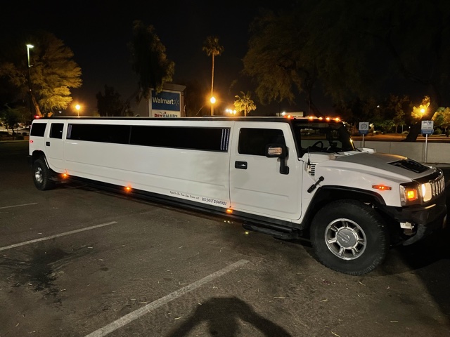 A white limo parked in the parking lot at night.